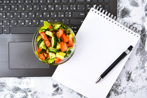 Collation de déjeuner d'affaires sain au bureau avec salade de légumes, cahier vide et stylo