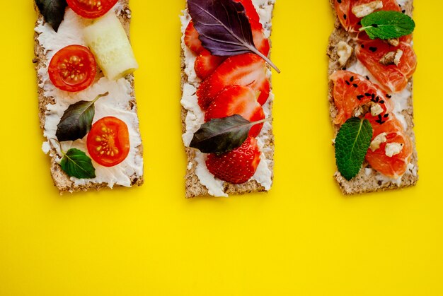 Collation santé avec pain croustillant, fromage à la crème, fraise, pamplemousse, tomate et concombre sur fond jaune