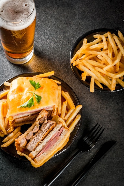 Collation traditionnelle portugaise. Sandwich Francesinha de pain, fromage, porc, jambon, saucisses, sauce à la bière à la tomate et frites. Avec un verre de bière et de pommes de terre. Sur tableau noir. Espace copie