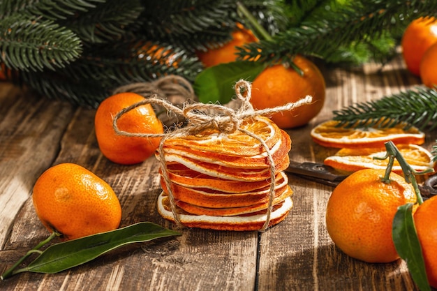 Collation de tranches d'oranges sèches. Agrumes séchés pour les décorations de Noël. Mandarines avec feuilles, branches de sapin, ciseaux et fil. Fond en bois, concept rustique, espace de copie