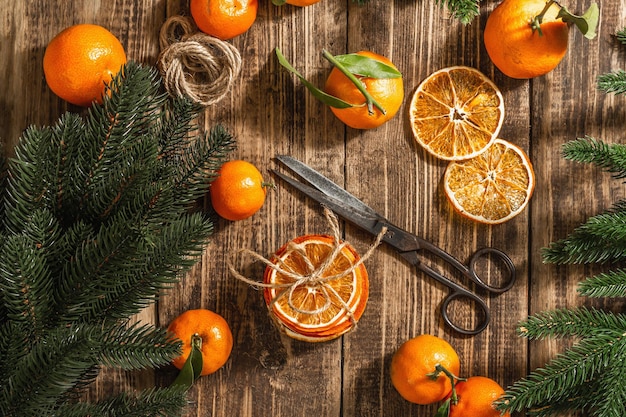 Collation de tranches d'oranges sèches. Agrumes séchés pour les décorations de Noël. Mandarines avec feuilles, branches de sapin, ciseaux et fil. Fond en bois, concept rustique, vue de dessus