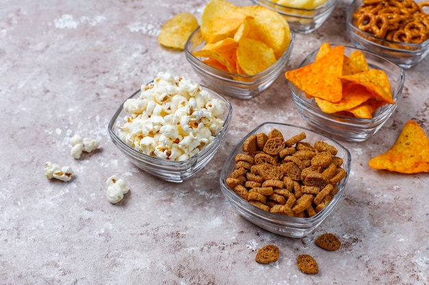 Collations salées. Bretzels, chips, crackers, pop-corn dans des bols. Produits malsains. nourriture mauvaise pour la figure, la peau, le cœur et les dents. Assortiment d'aliments riches en glucides