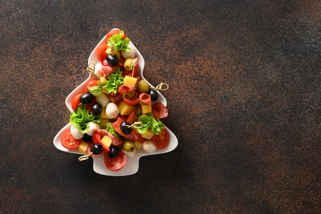 Des collations de vacances sous forme de canapés en forme de plaque d'arbre de Noël pour la fête de Noël isolée sur brun.