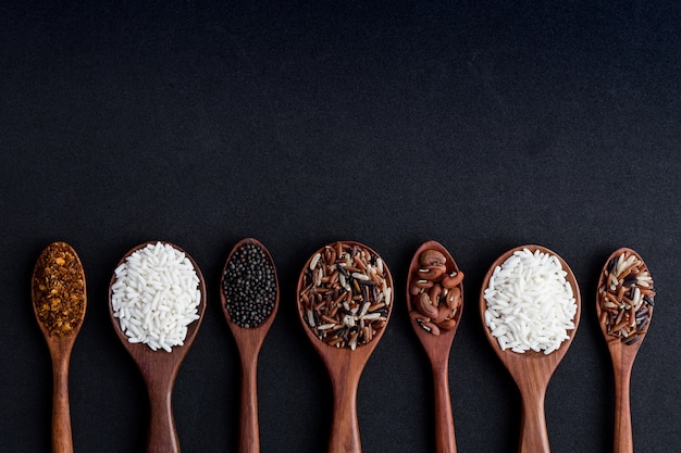 collection de grains dans une cuillère en bois sur fond noir.