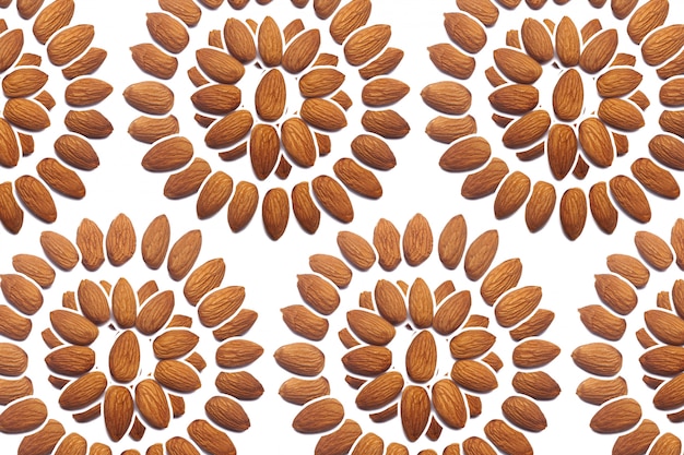 Une collection de noix d'amande décortiquées se présente sous la forme d'un cercle ou d'un soleil sur un mur blanc isolé. Motif d'amandes décortiquées