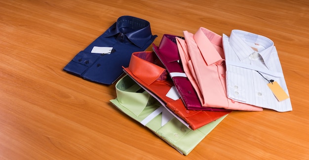 Collection de nouvelles chemises colorées pour hommes, pliées avec des étiquettes attachées et déployées sur une surface en bois
