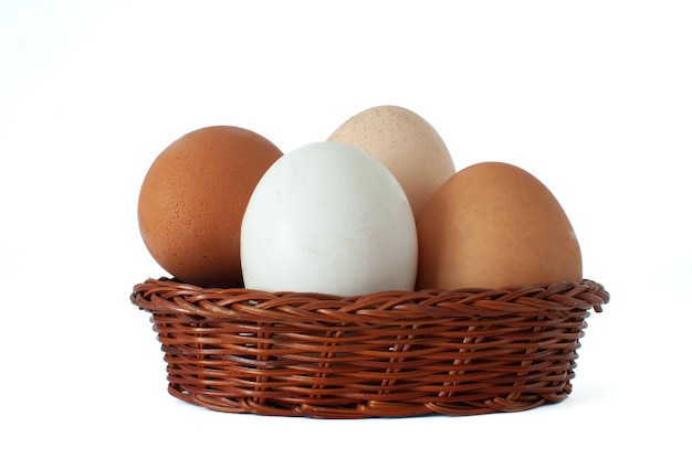 Collection d'œufs de poule de ferme biologique blancs et bruns dans un panier en osier brun, isolés sur blanc.