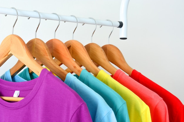 collection de t-shirts colorés arc-en-ciel suspendus sur un cintre en bois sur un porte-vêtements