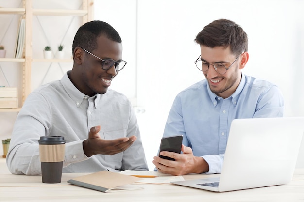 Un collègue aidant un autre avec sa tâche montrant la solution sur le smartphone au bureau du bureau