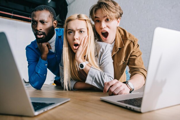 Photo des collègues d'affaires multiculturels choqués regardant sur l'écran de leur ordinateur portable