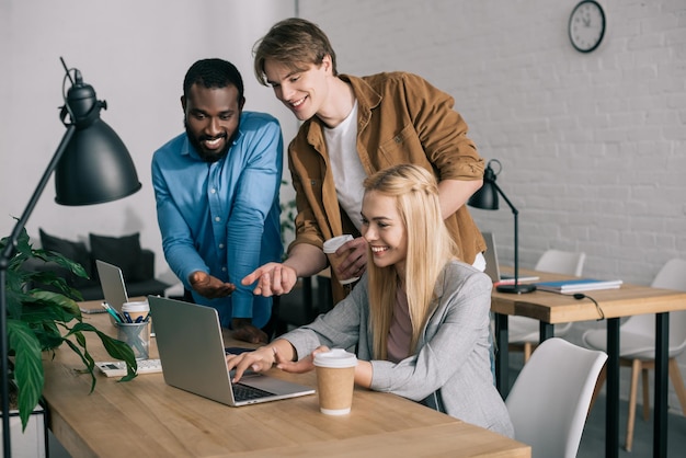 Des collègues d'affaires multiculturels souriants parlent et regardent sur un ordinateur portable