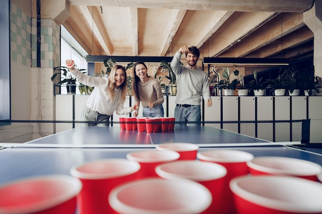 Collègues de jeunes gens jouant de la bière pong dans un bureau moderne