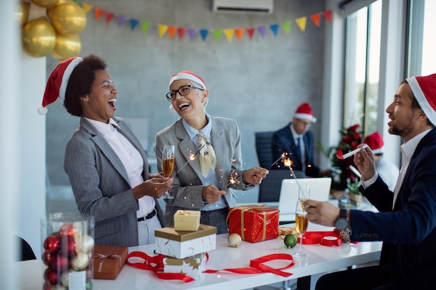 Photo des collègues joyeux boivent du champagne et s'amusent avec des étincelles lors de la fête de noël au bureau