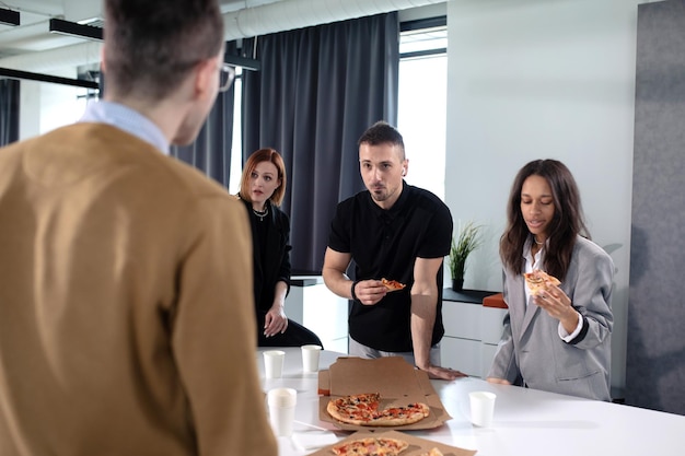 Des collègues mangent de la pizza au bureau pendant le déjeuner