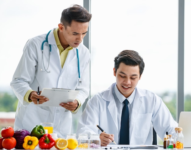 Collègues masculins asiatiques en uniforme médical travaillant ensemble sur une table avec des fruits pendant le travail dans une clinique moderne