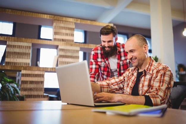 Collègues masculins souriant tout en discutant sur ordinateur portable