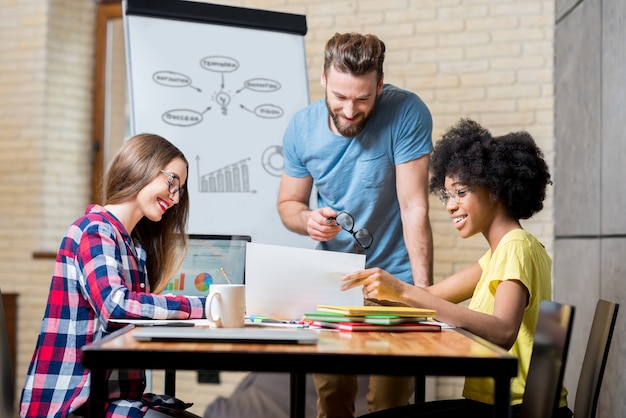 Des collègues multiethniques vêtus avec désinvolture de vêtements colorés travaillant pendant la réunion au bureau avec un ordinateur portable, des documents et un tableau blanc