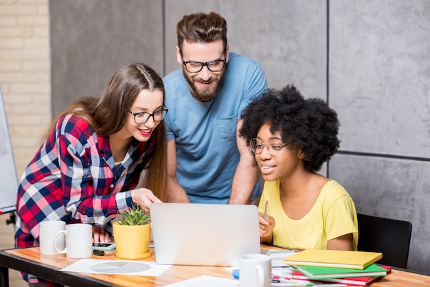 Des collègues multiethniques vêtus avec désinvolture de vêtements colorés travaillant pendant la réunion au bureau avec un ordinateur portable et des documents