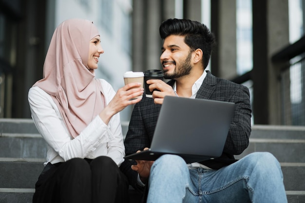 Collègues musulmans portant un toast avec des tasses de café à l'extérieur