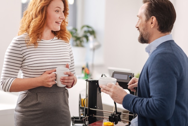 Collègues ravis et amicaux positifs qui se parlent et prennent un café tout en étant au travail