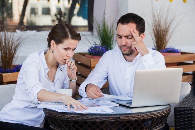 Collègues de travail masculins et féminins travaillant ensemble sur un problème difficile au café en plein air. Ils ont tendu l'expression sur leurs visages