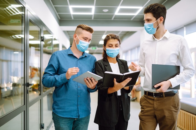 Collègues de travail portant des masques protecteurs dans un bureau moderne discutant ensemble de problèmes de travail.