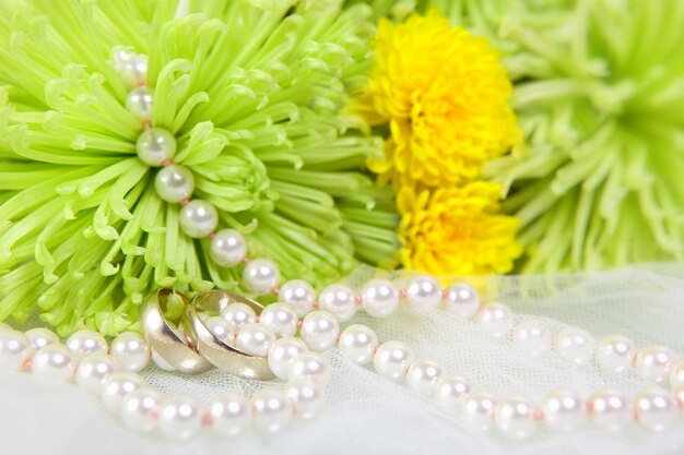 Collier blanc de perles, alliances et bouquet de chrysanthèmes sur voile blanc