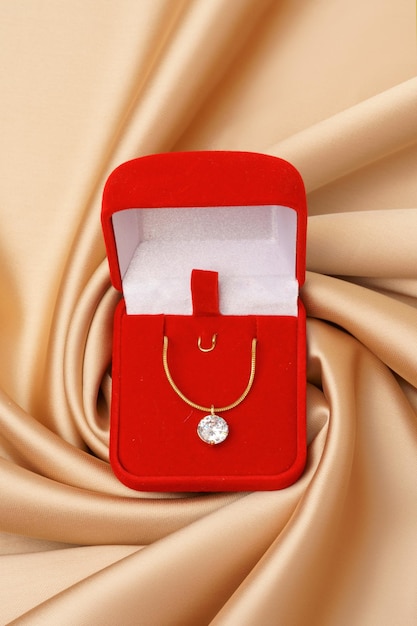 Un collier d'or avec un pendentif en diamant dans une boîte rouge sur fond de soie