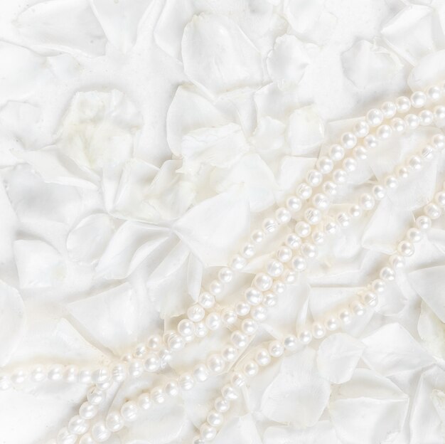 Collier de perles sur fond de pétales de roses blanches idéal pour les cartes de voeux pour anniversaire de mariage