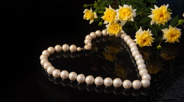 Collier de perles en forme de cœur et de roses sur une surface sombre et humide, mise au point sélective.