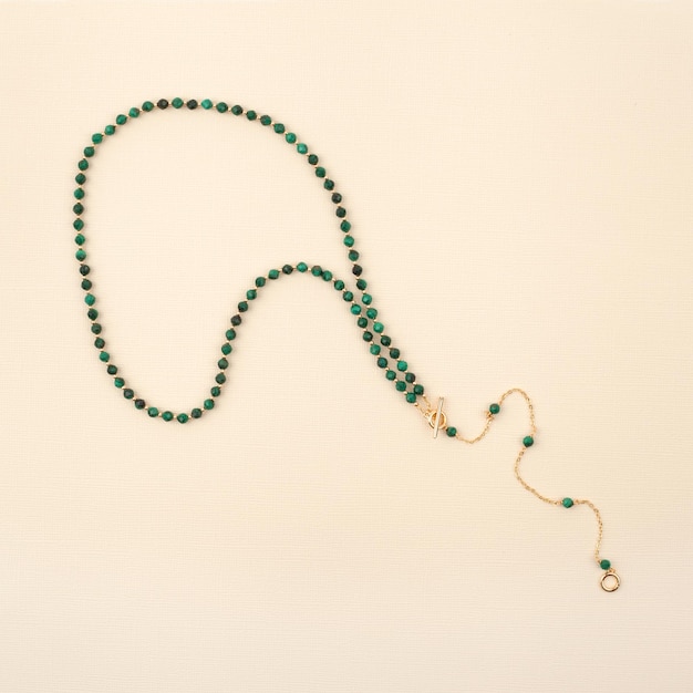 Collier pour femme de pierres précieuses de malachite verte sur fond texturé beige xDTop view