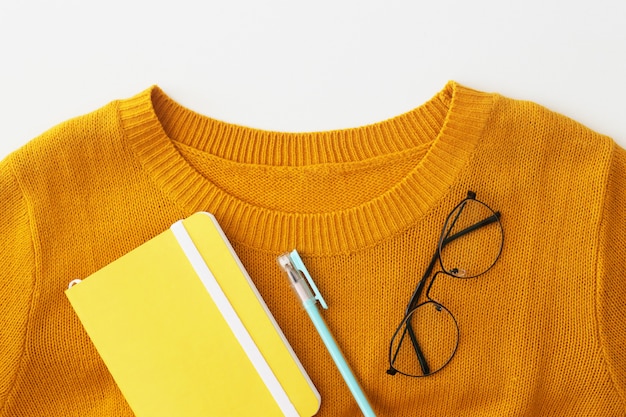 Un collier d&#39;un pull jaune vif avec un carnet, un stylo et des lunettes