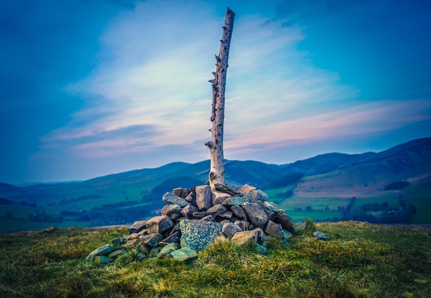 Colline écossaise avec cairn et poteau en bois au coucher du soleil