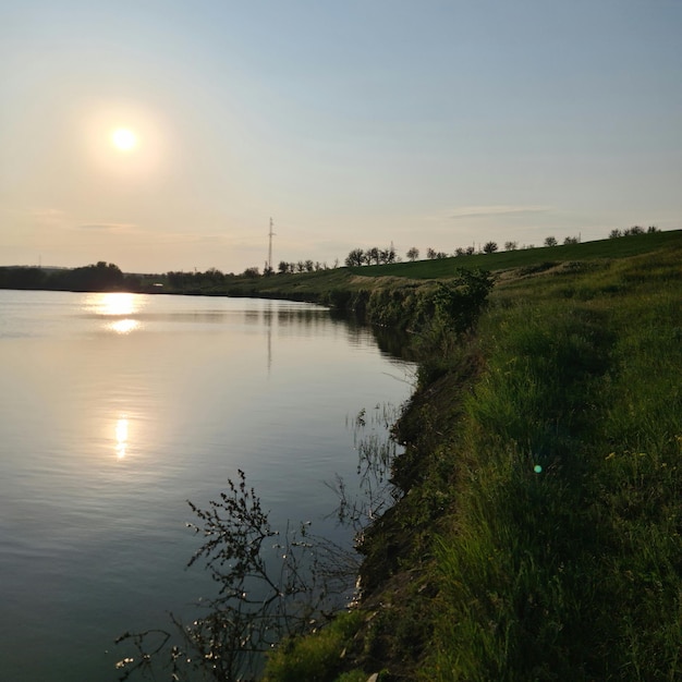 Une colline herbeuse à côté d'un lac avec un coucher de soleil derrière elle.