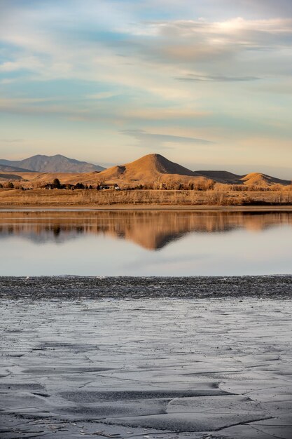 Photo une colline se reflète dans un lac partiellement gelé avec de la glace au premier plan