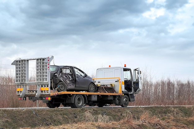 Une collision latérale laisse une voiture dans le besoin d'une dépanneuse la voiture est gravement endommagée et peut être irréparable une hatchback japonaise noire moderne est tirée par une dépanneure sur l'autoroute