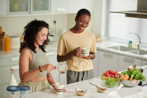 Colocataires joyeux buvant du café et préparant le petit-déjeuner dans la cuisine