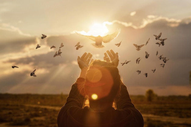 Les colombes volent dans les mains de la femme dans le contexte d'un coucher de soleil ensoleillé pendant la prière