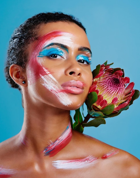 Coloré comme une fleur Studio portrait d'une belle jeune femme couverte de peinture pour le visage posant sur un fond bleu