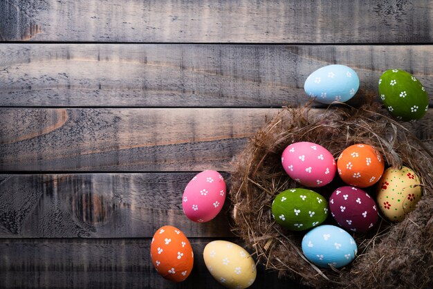 Coloré des oeufs de Pâques en nid et plume sur fond en bois.