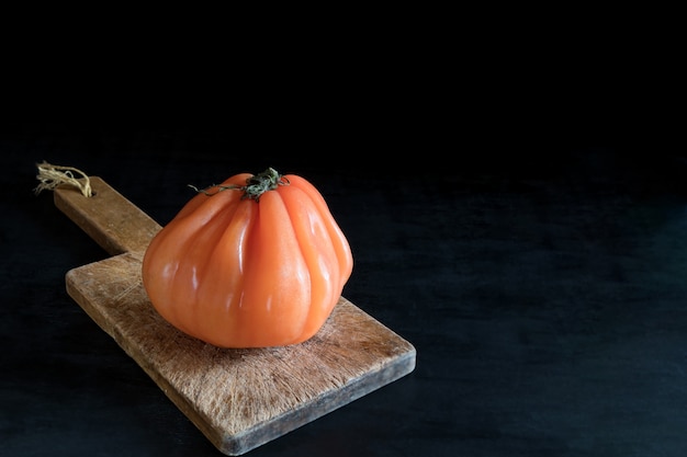 Coloré tomate laide juteuse sur une planche à découper en bois sur une table noire, style rustique et discret