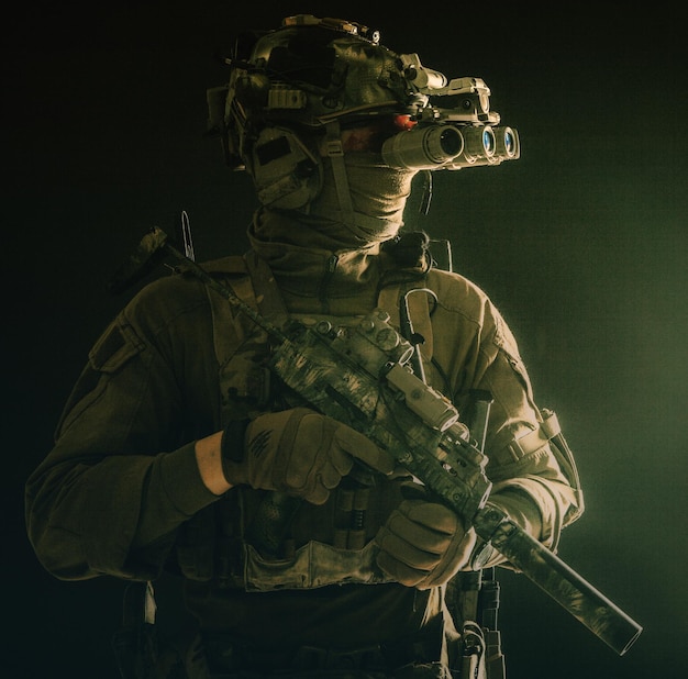 Combattant de groupe tactique des forces spéciales de l'armée se déplaçant dans l'obscurité à l'aide d'un casque radio regardant à travers un dispositif d'imagerie thermique à vision nocturne à quatre lentilles sur une petite mitraillette armée d'un casque avec silencieux