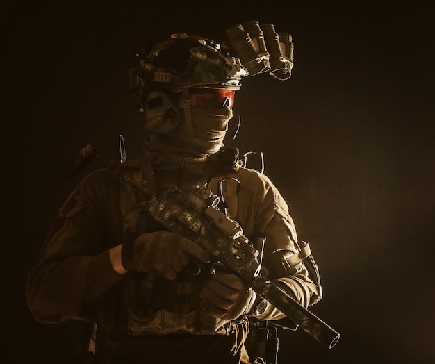 Combattant de groupe tactique des forces spéciales de l'armée se déplaçant dans l'obscurité à l'aide d'un casque radio regardant à travers un dispositif d'imagerie thermique à vision nocturne à quatre lentilles sur une petite mitraillette armée d'un casque avec silencieux