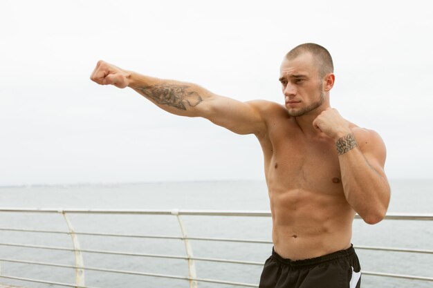 Combattant masculin musclé avec un torse nu faisant des coups de poing sur la plage