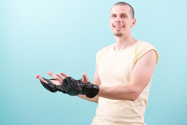 Un combattant MMA heureux dans des gants noirs et une chemise jaune debout sur un fond bleu et montre avec deux mains sur l'espace de copie Confiant Champion Gants Endurance Fighting Combat Smile