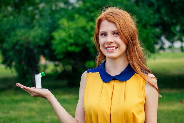 Combattre l'asthme et la bronchite. active joyeuse belle jeune femme norvégienne irlandaise rousse au gingembre vêtue d'une robe jaune tenant l'inhalateur à la main dans le parc d'été. concept d'allergie printanière