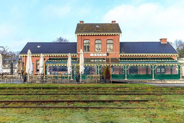 Photo comme limbourg belgique décembre 17 2023 façade du restaurant asch dans le bâtiment de l'ancienne gare terrasse avec chaises et tables voies désaffectées devant le jour nuageux