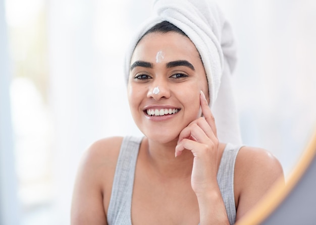 Commencez votre journée du bon pied Photo d'une jeune femme heureuse appliquant une crème hydratante pour le visage devant son miroir