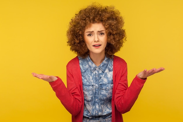 Photo comment peux-tu. portrait d'une femme agacée aux cheveux bouclés moelleux en tenue décontractée levant les mains dans un geste indigné, se disputant, ayant des conflits. studio d'intérieur tourné isolé sur fond jaune