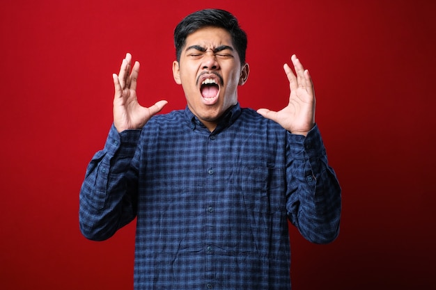 Comment peux-tu? Portrait d'un homme asiatique frustré et agacé debout avec les mains levées, demandant pourquoi. studio intérieur tourné sur fond rouge